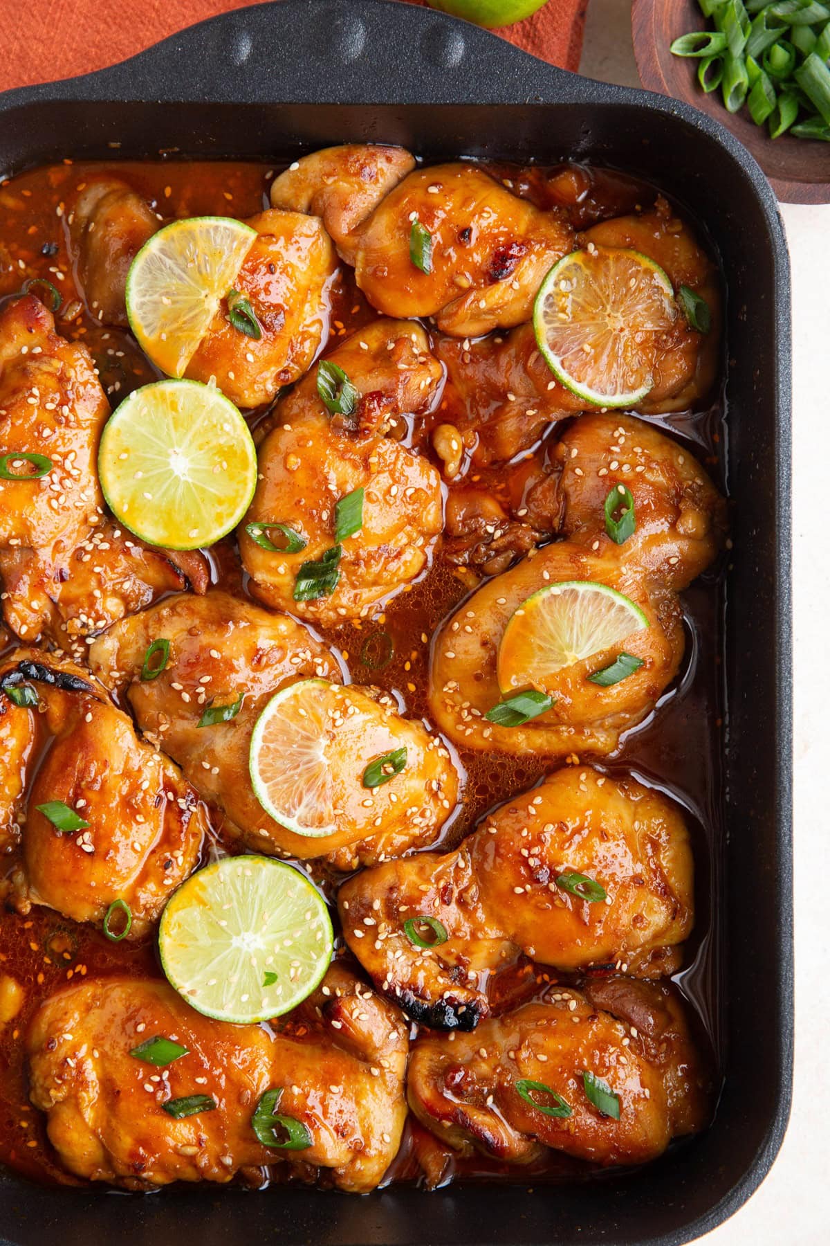 Korean BBQ chicken in a large roasting pan, fresh out of the oven. Sprinkled with green onions and sliced limes on the chicken.