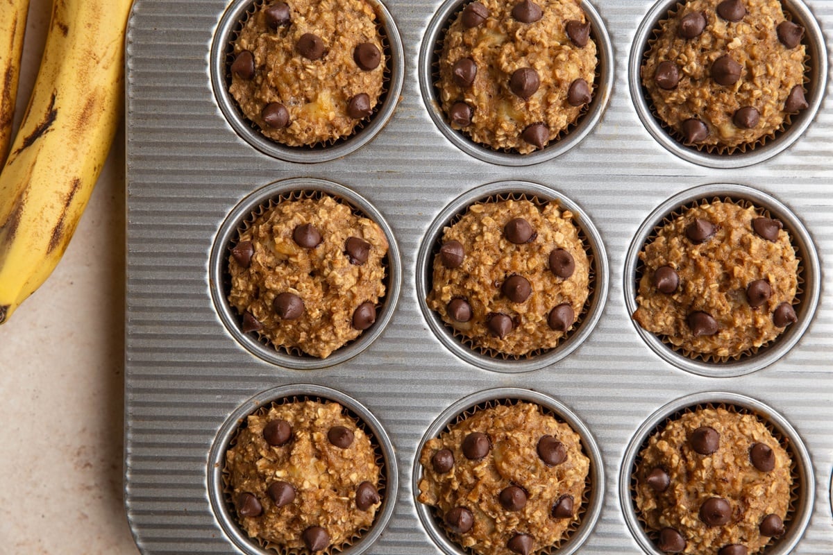 Banana baked oatmeal muffins in a muffin tin, fresh out of the oven. With ripe bananas to the side.