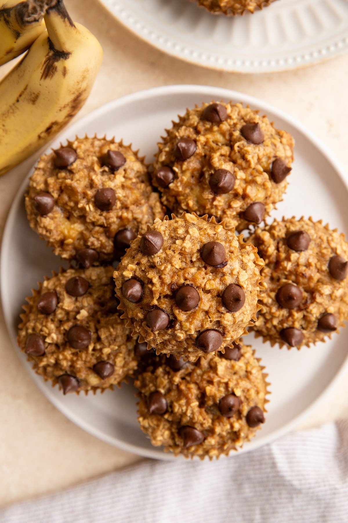Plate of banana oatmeal muffins with ripe bananas and a napkin to the side.