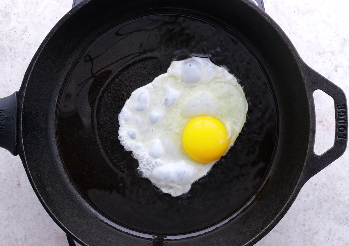 Sunny side up egg cooking in a cast iron skillet.
