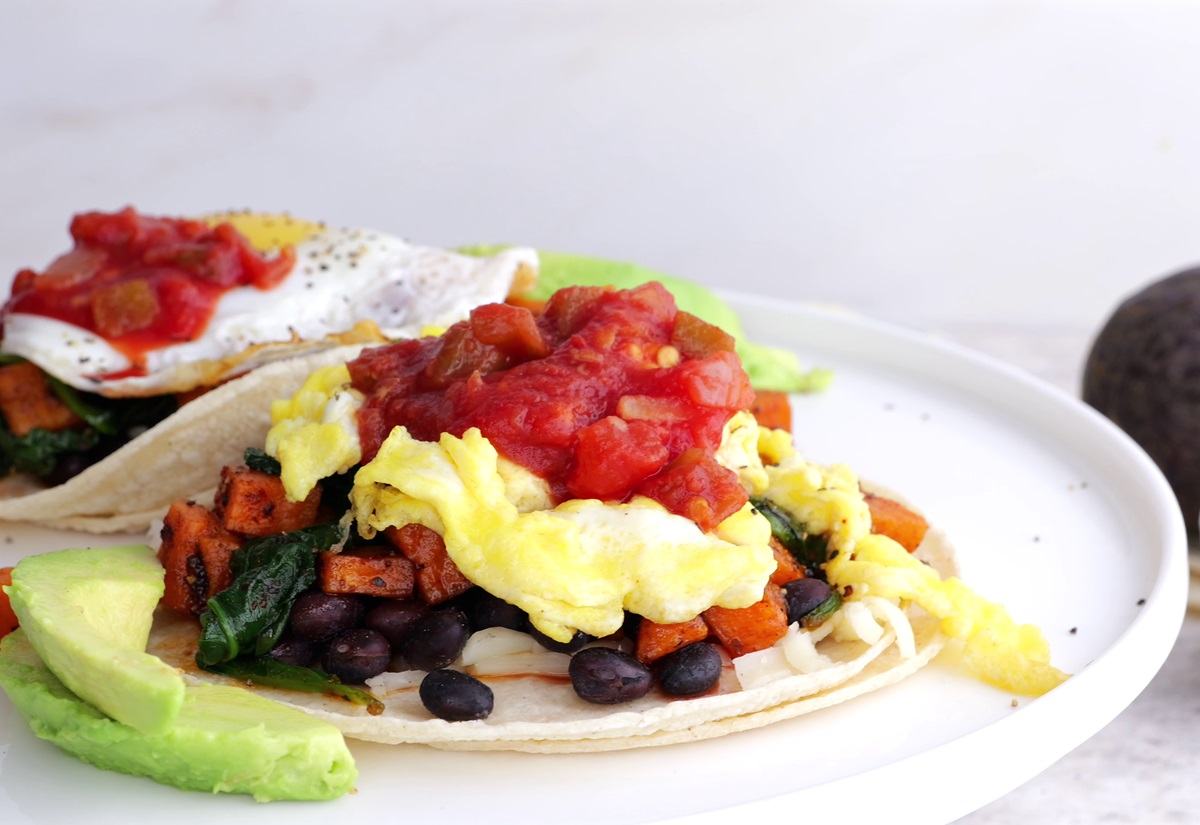 Two breakfast tacos on a plate with scrambled eggs and salsa.