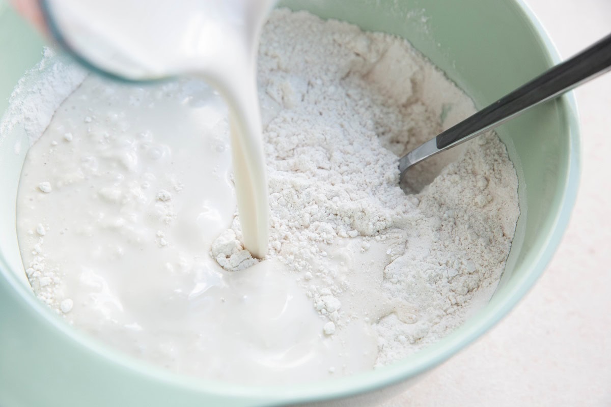 Pouring coconut milk into a bowl with dry ingredients.