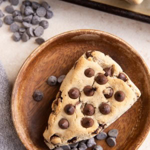 Chocolate chip scone on a wooden plate with the baking sheet of the rest of the scones.