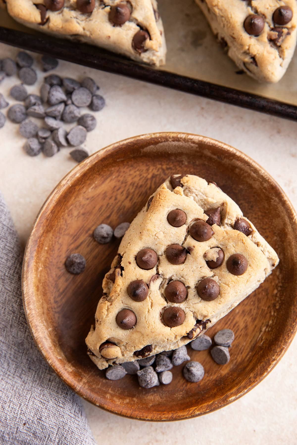 Chocolate chip scone on a wooden plate with the baking sheet of the rest of the scones.