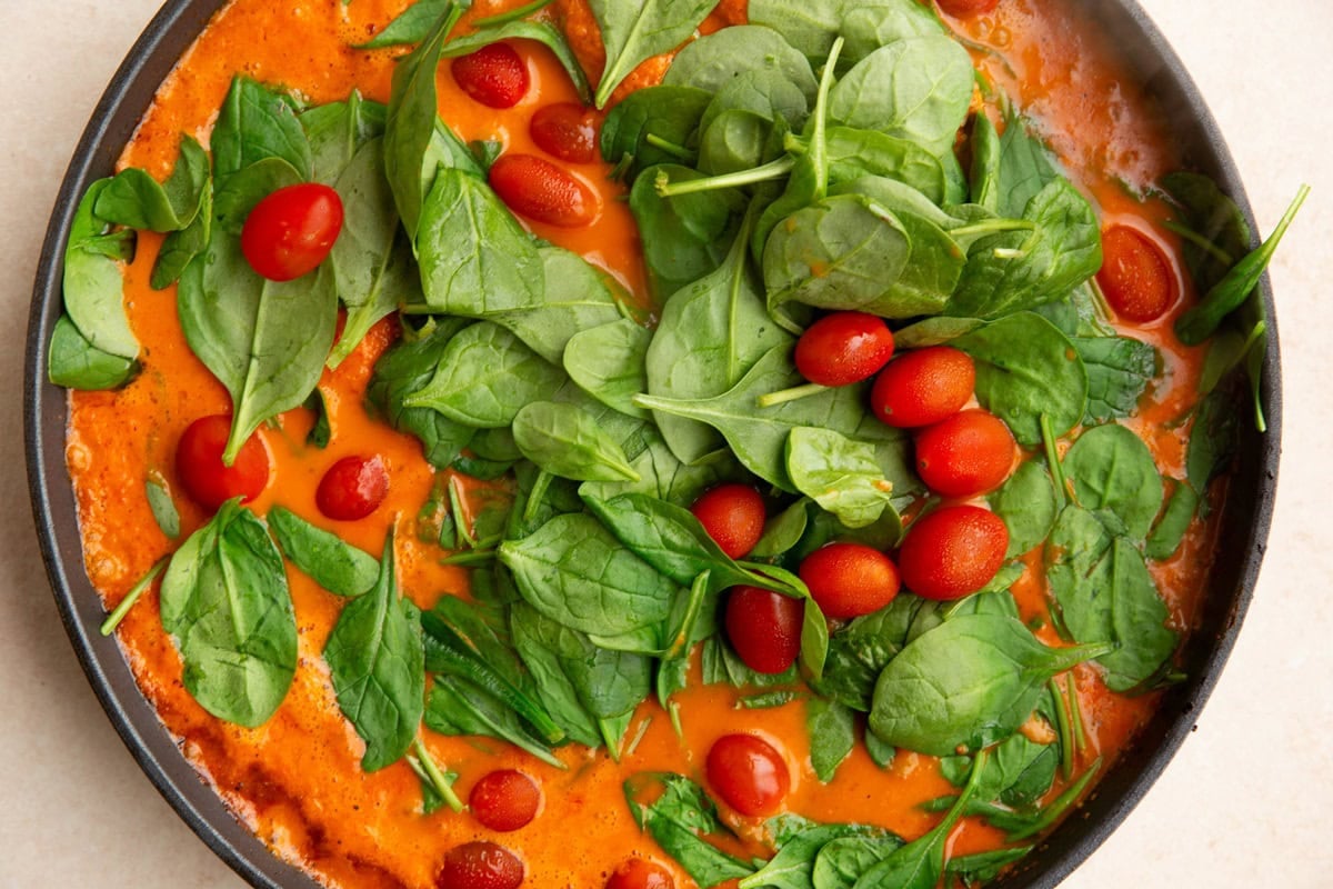 spinach and cherry tomatoes on top of roasted red pepper chicken in a skillet.