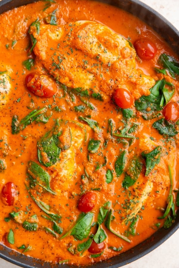 Skillet with creamy roasted red pepper chicken in creamy sauce with spinach and cherry tomatoes.