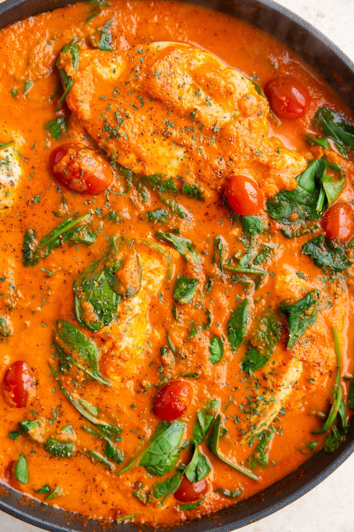 Skillet with creamy roasted red pepper chicken in creamy sauce with spinach and cherry tomatoes.