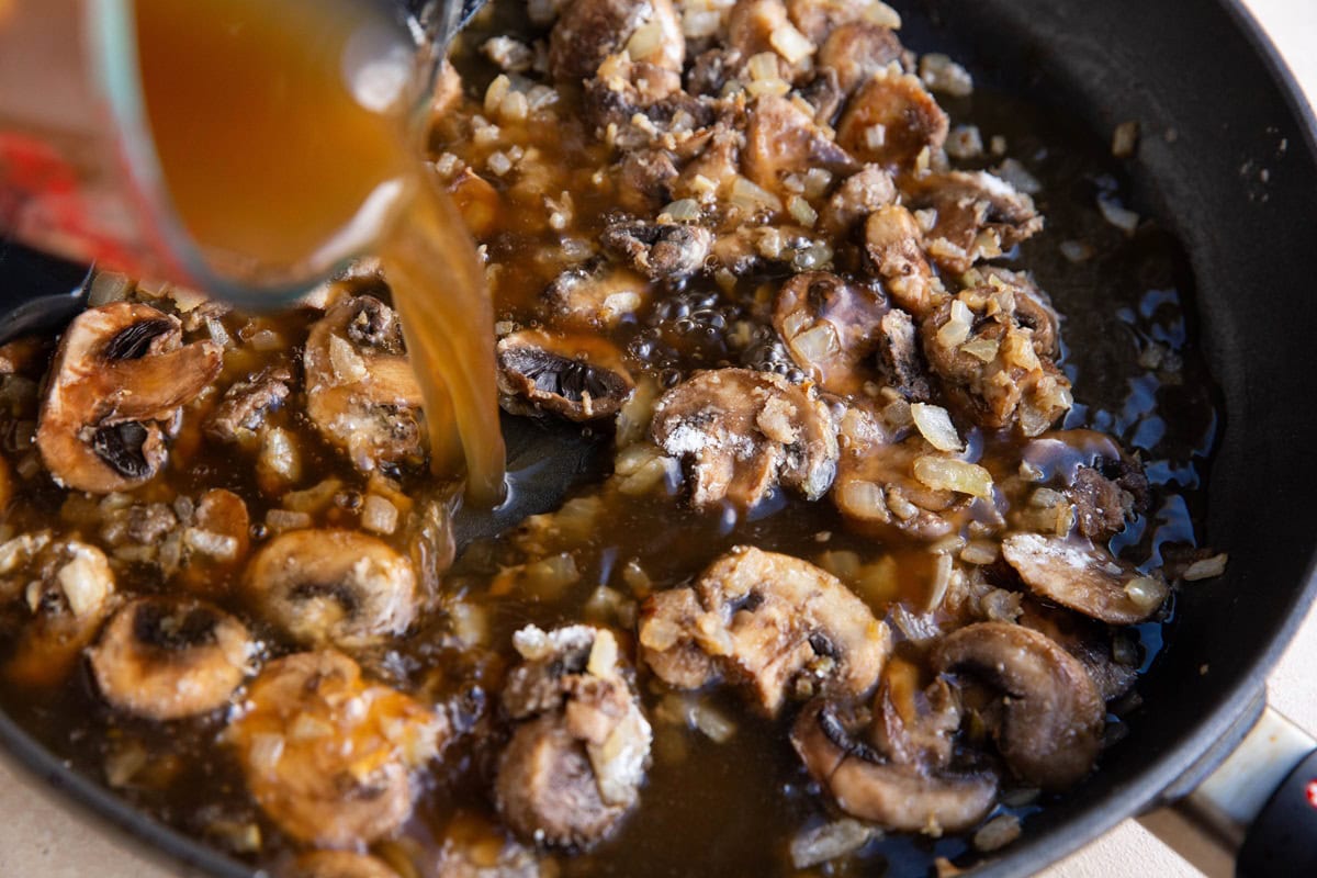 Pouring beef broth into the skillet with the mushrooms and onions.