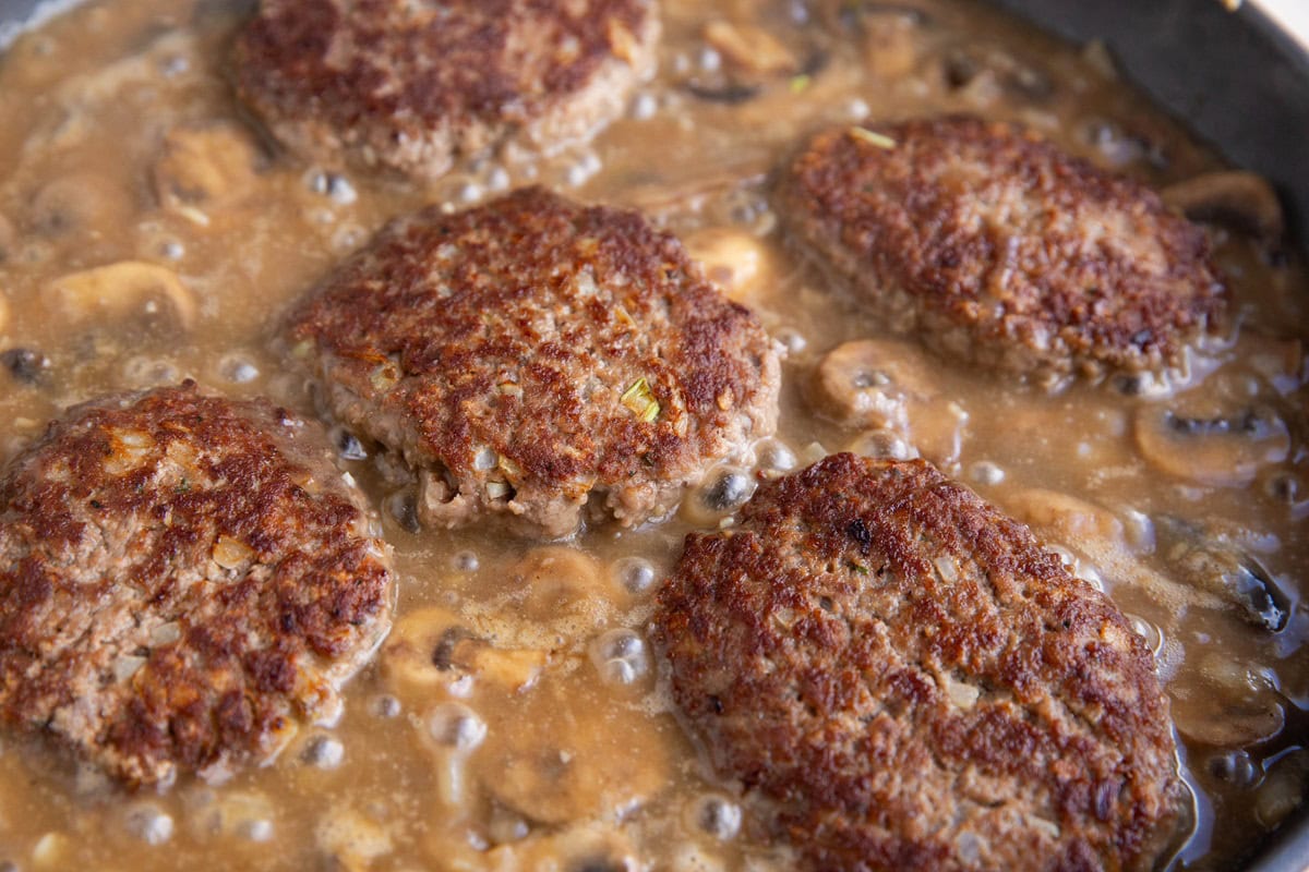 Hamburger steaks cooking in gravy.