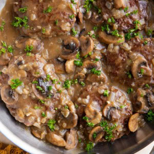 Salisbury steak in a stainless steel skillet with parsley sprinkled on top.