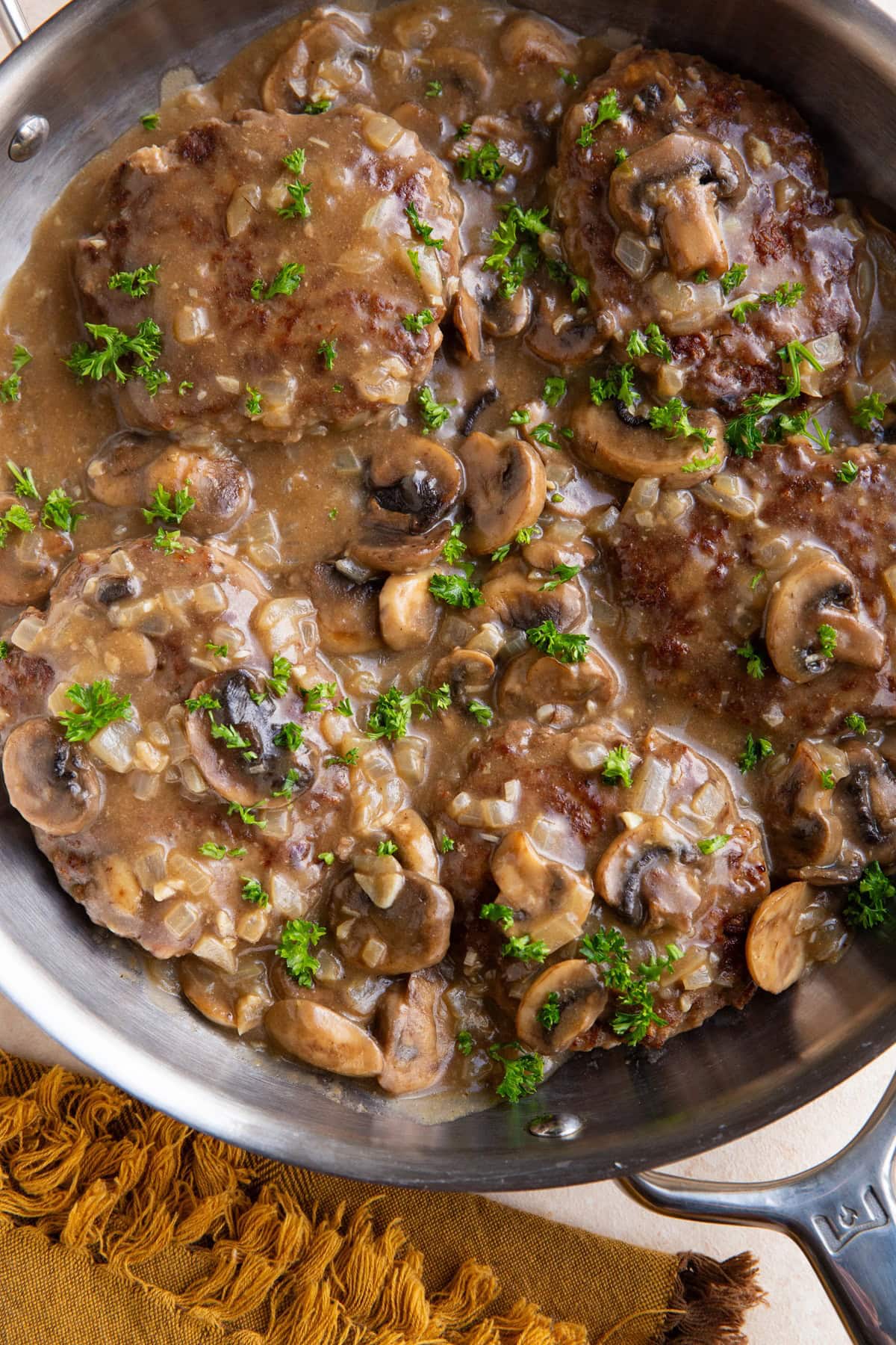 Salisbury steak in a stainless steel skillet with parsley sprinkled on top.