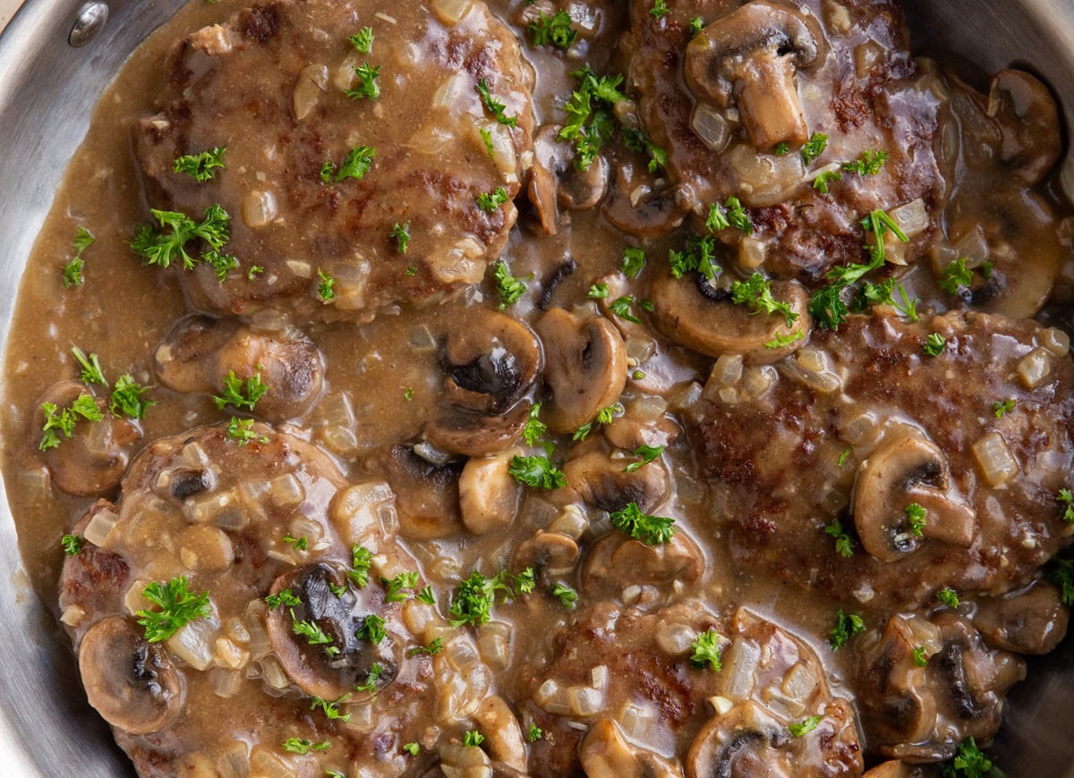 Stainless steel skillet of salisbury steaks with mushroom gravy, ready to serve.