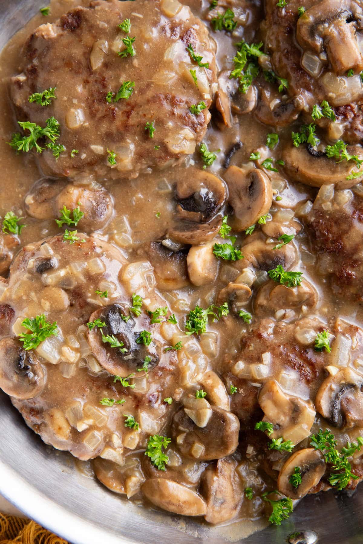 Salisbury steaks in a stainless steel skillet, smothered in gravy.