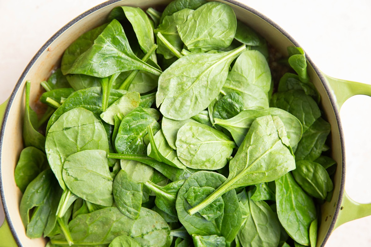 Baby spinach on top of soup ingredients in a large pot.