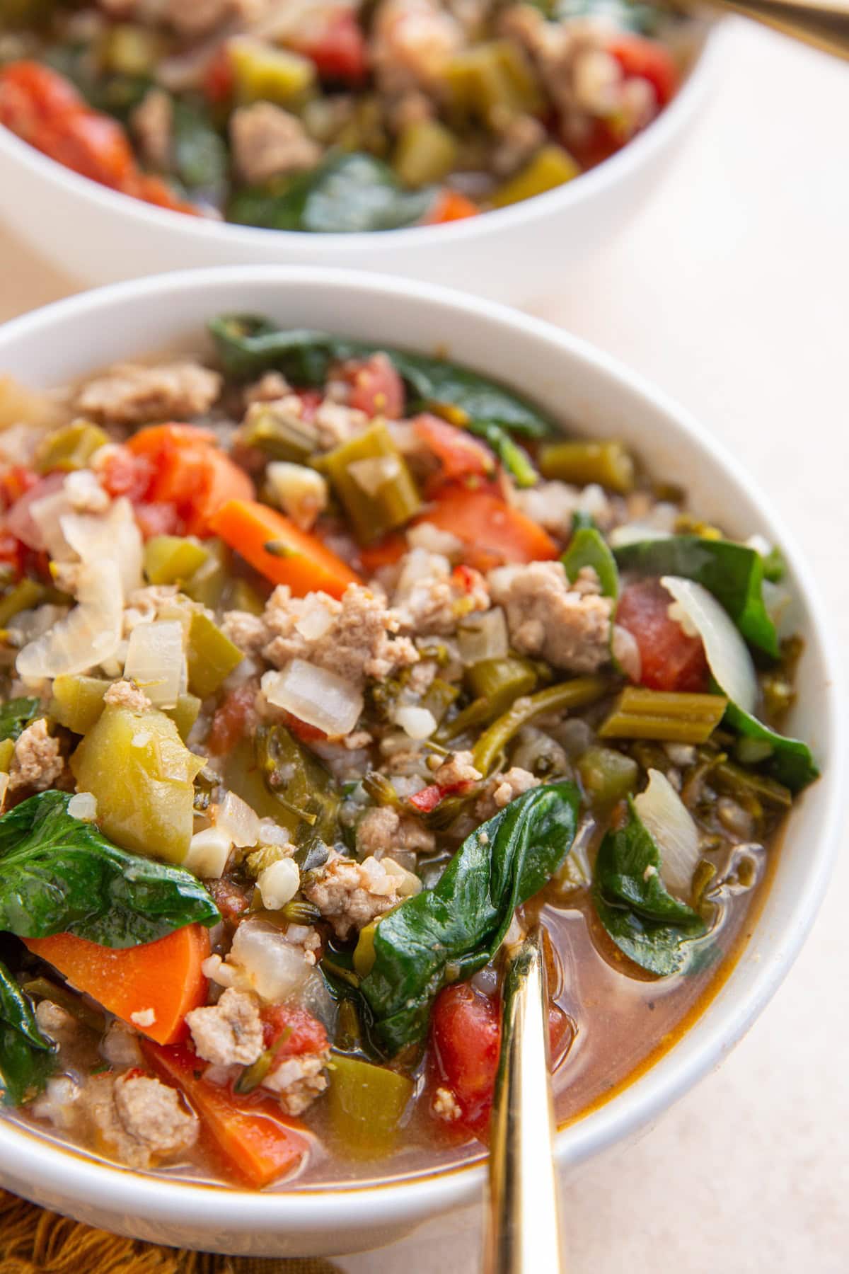 Two big white bowls full of ground turkey soup with a golden spoon, ready to eat.