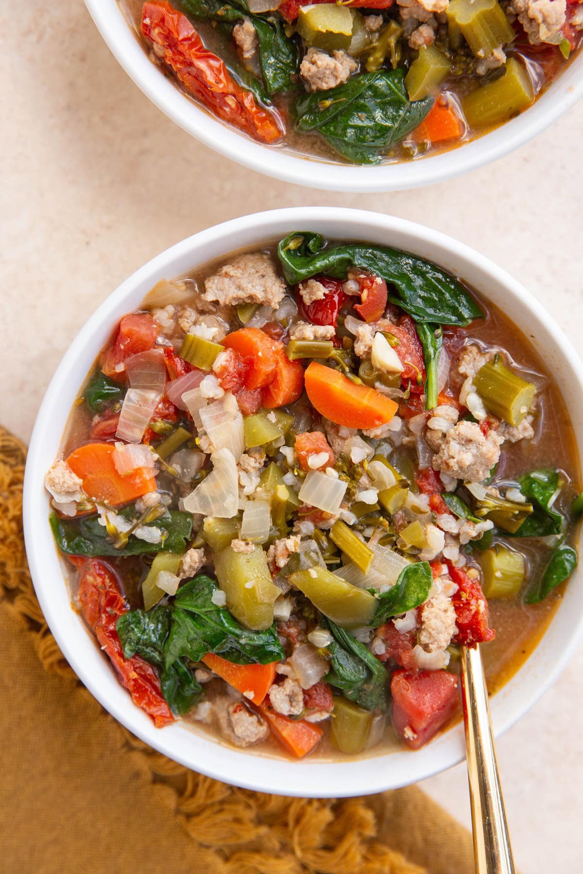 Two white bowls full of ground turkey and rice soup with fresh veggies and a golden napkin to the side with a gold spoon.