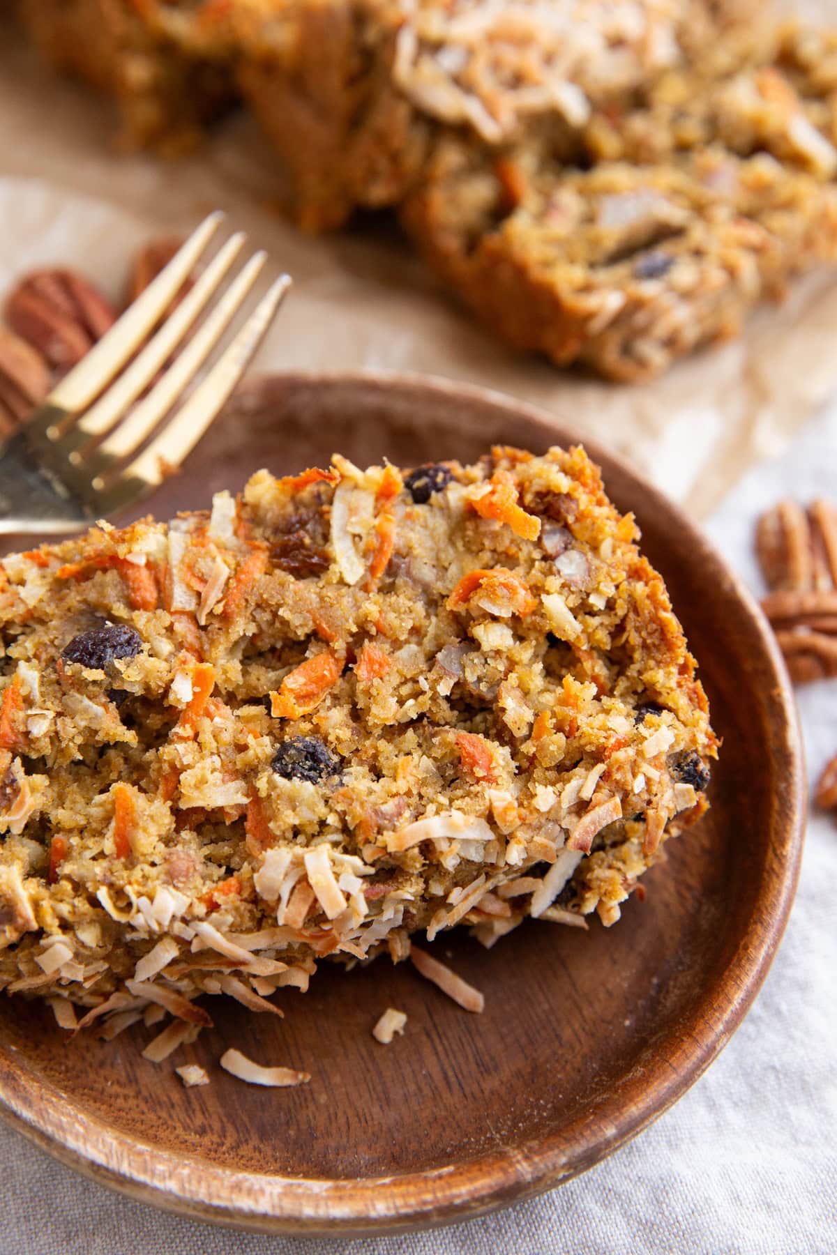 Slice of carrot cake bread on a plate with the rest of the loaf in the background.