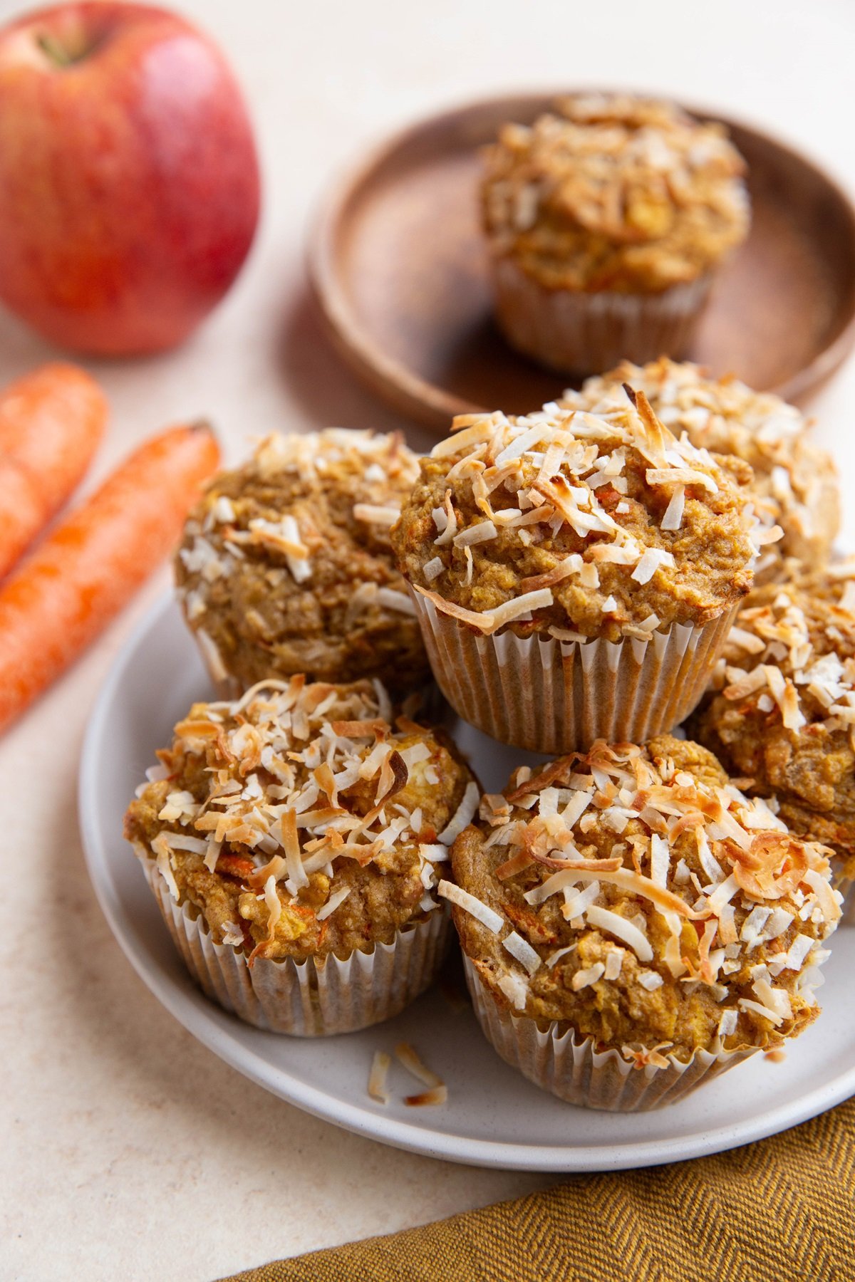 Plate of carrot muffins with fresh carrots and an apple in the background.