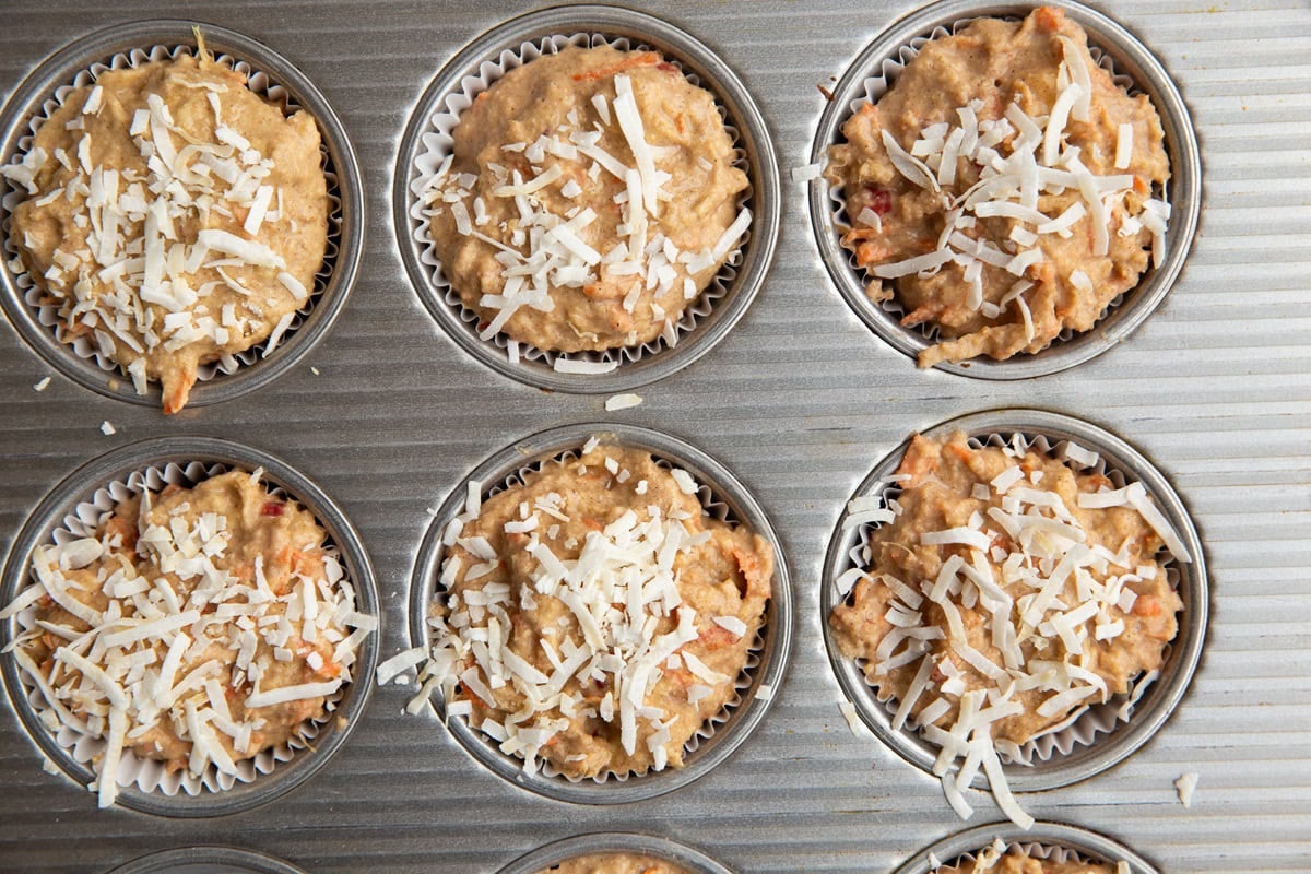 Muffin tray with muffin batter inside, sprinkled with flaked coconut.