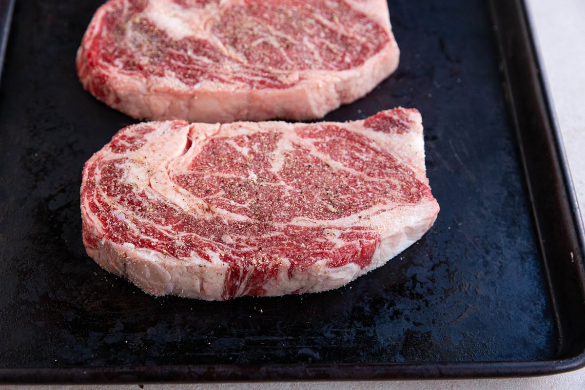 Raw steaks on a baking shet.