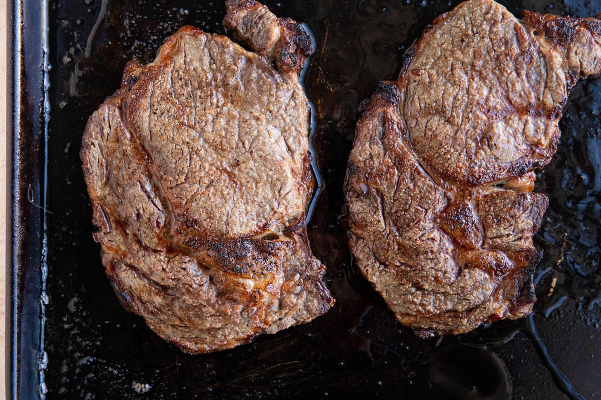 Ribeye steaks on a baking sheet, fresh out of the oven.