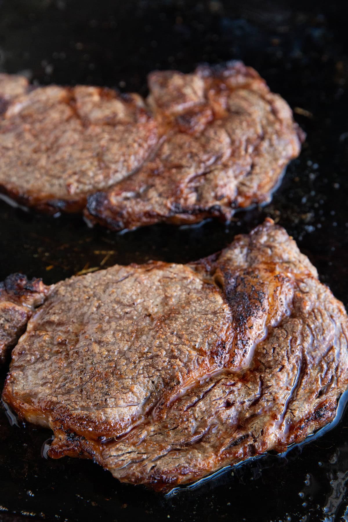 Two broiled ribeye steaks on a baking sheet, fresh out of the oven.