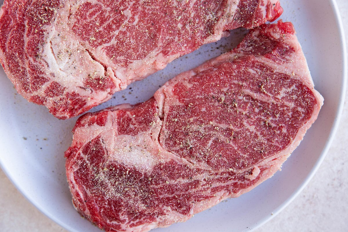 Boneless ribeye steaks seasoned on a plate, ready to cook.