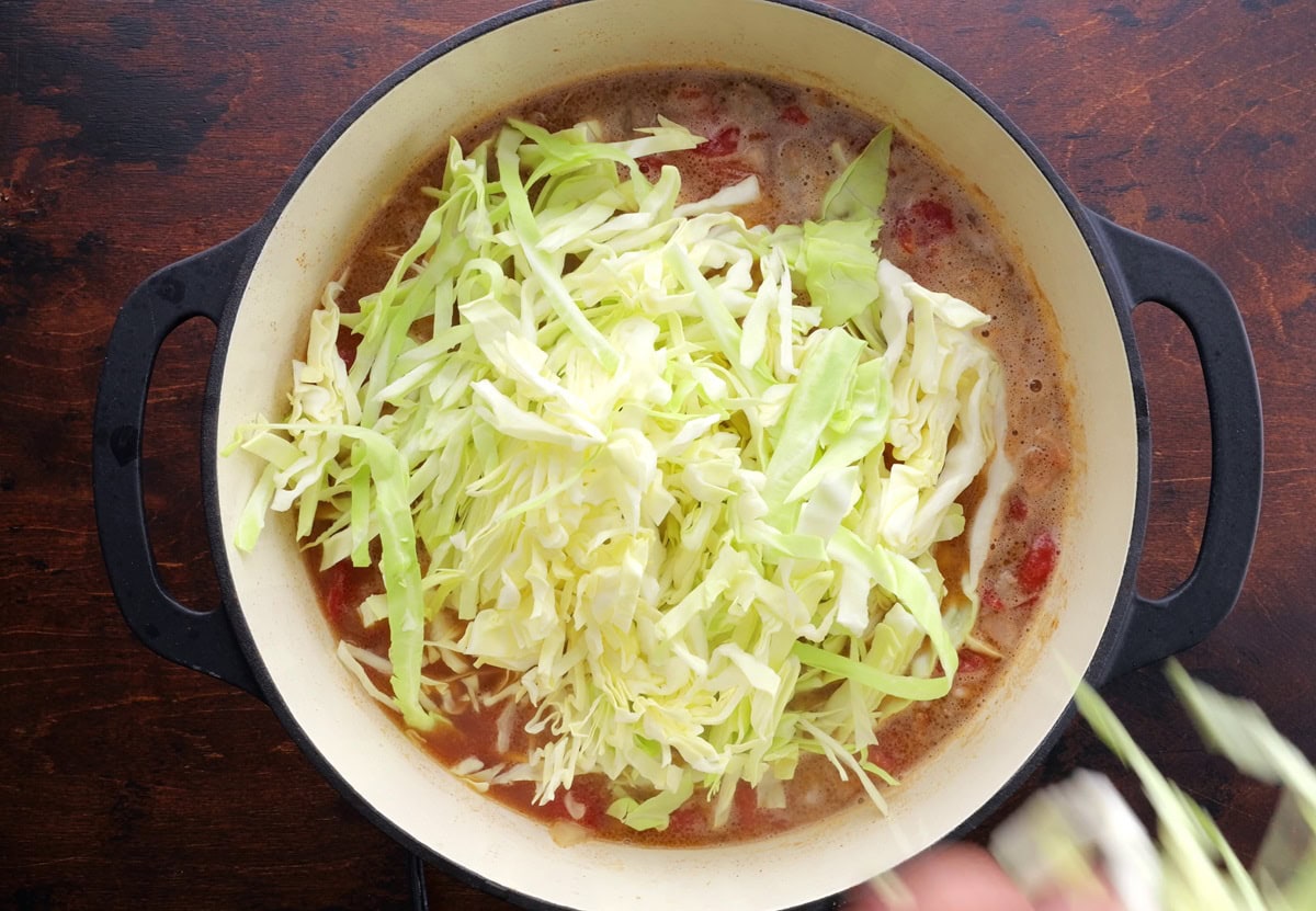 Cabbage on top of soup in a large pot, ready to be mixed in.