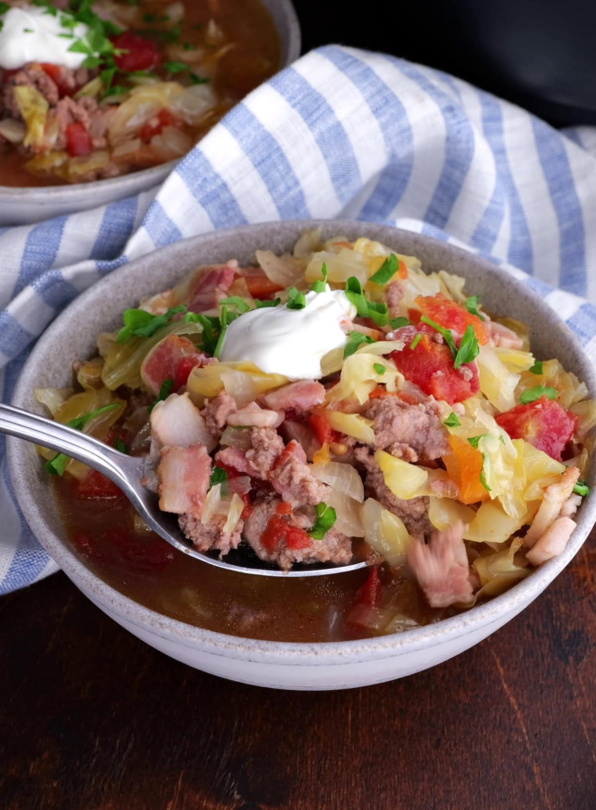 Two bowls full of sausage and cabbage soup with a spoon lifting a bite out.