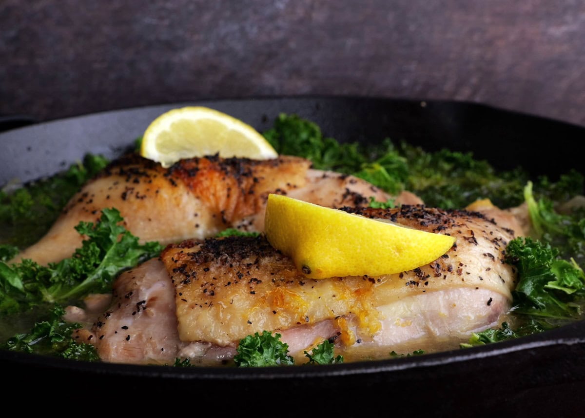 Completed braised chicken in a cast iron skillet with slices of lemon on top.