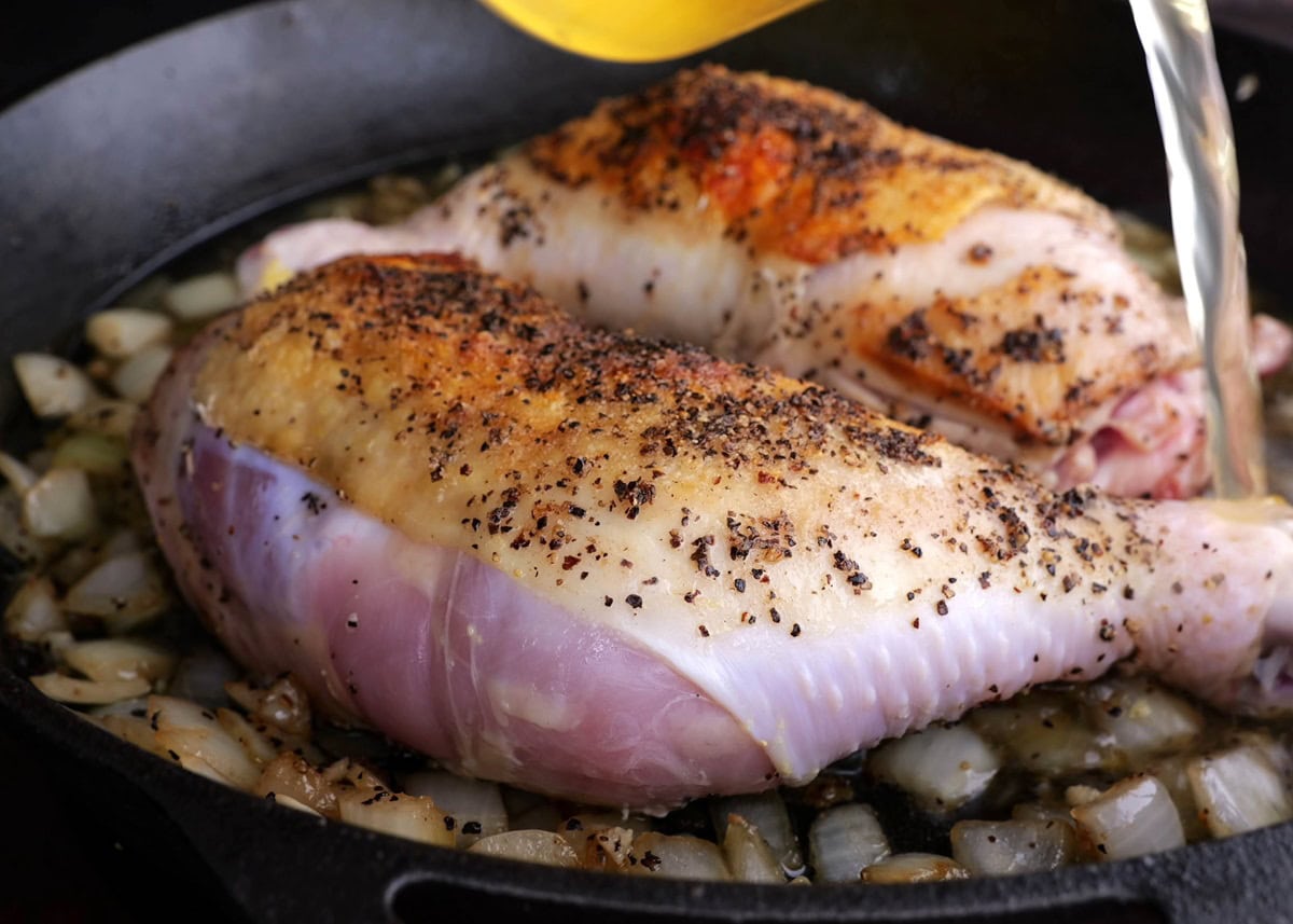 Pouring broth into a skillet with the golden brown chicken