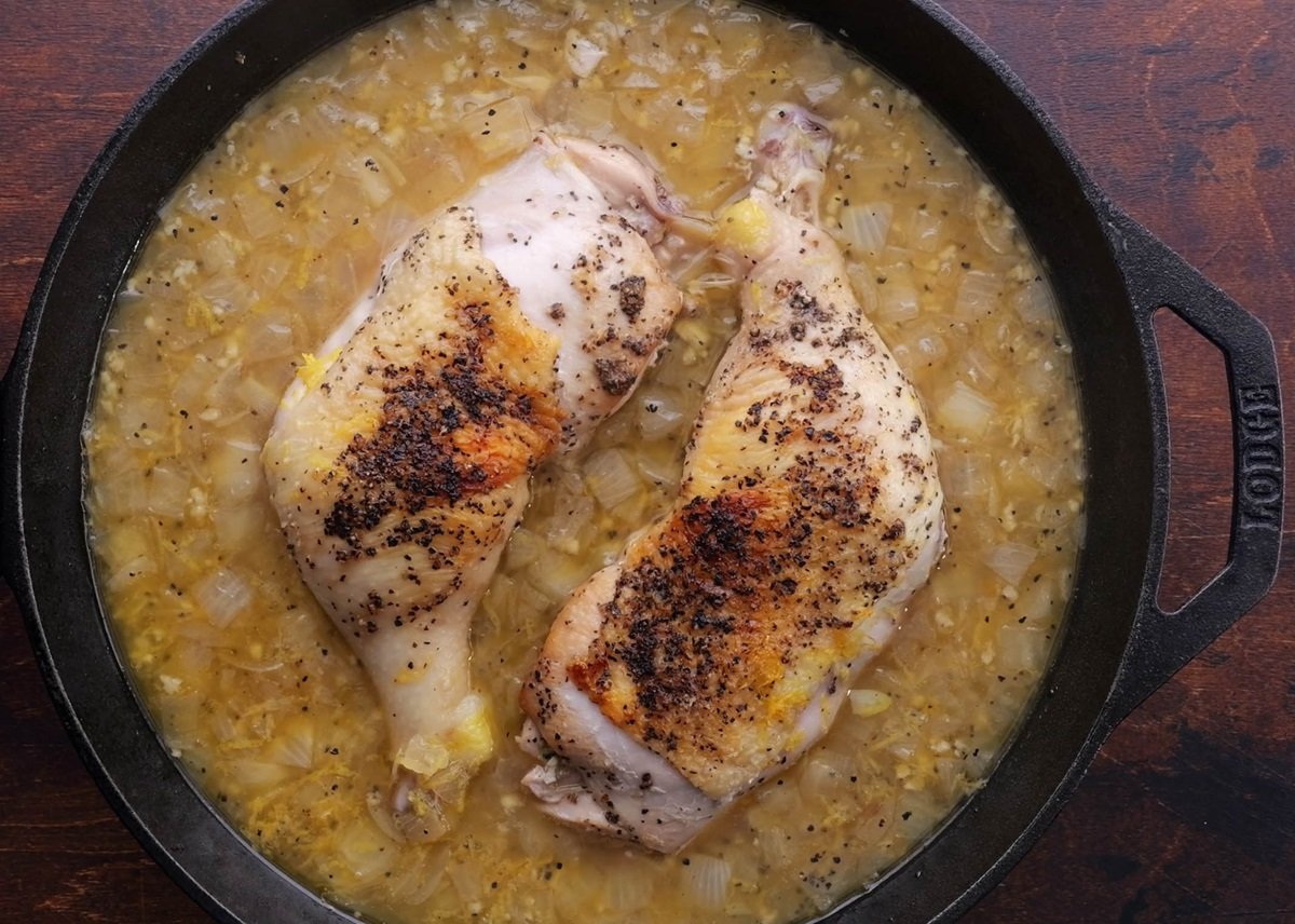 Chicken in a skillet with juices all around for braising.