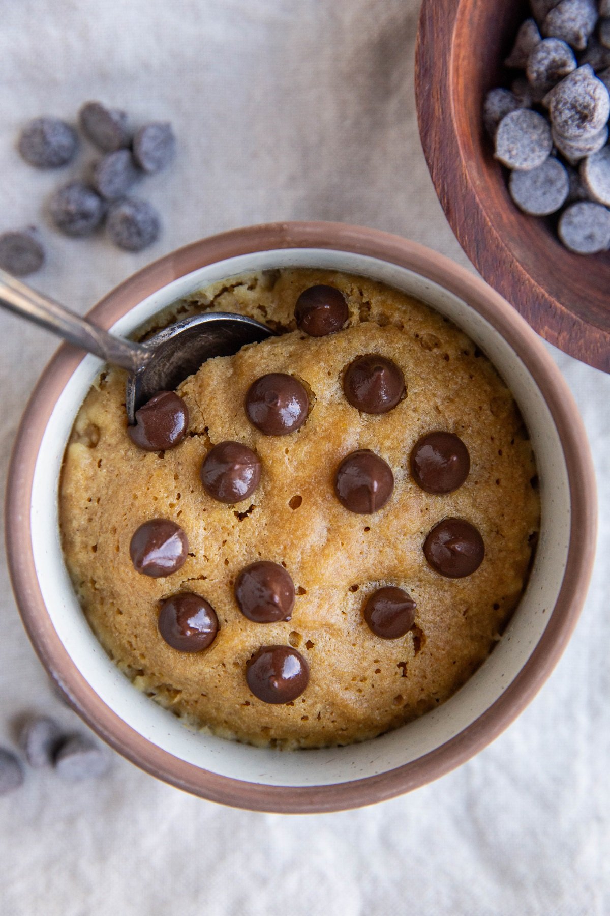 Peanut butter cookie in a mug with chocolate chips on top and a spoon dug in, ready to eat.