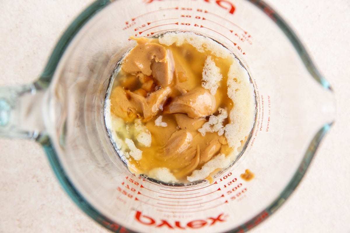 peanut butter, butter, and pure maple syrup in a measuring cup to make a peanut butter cookie in a mug.