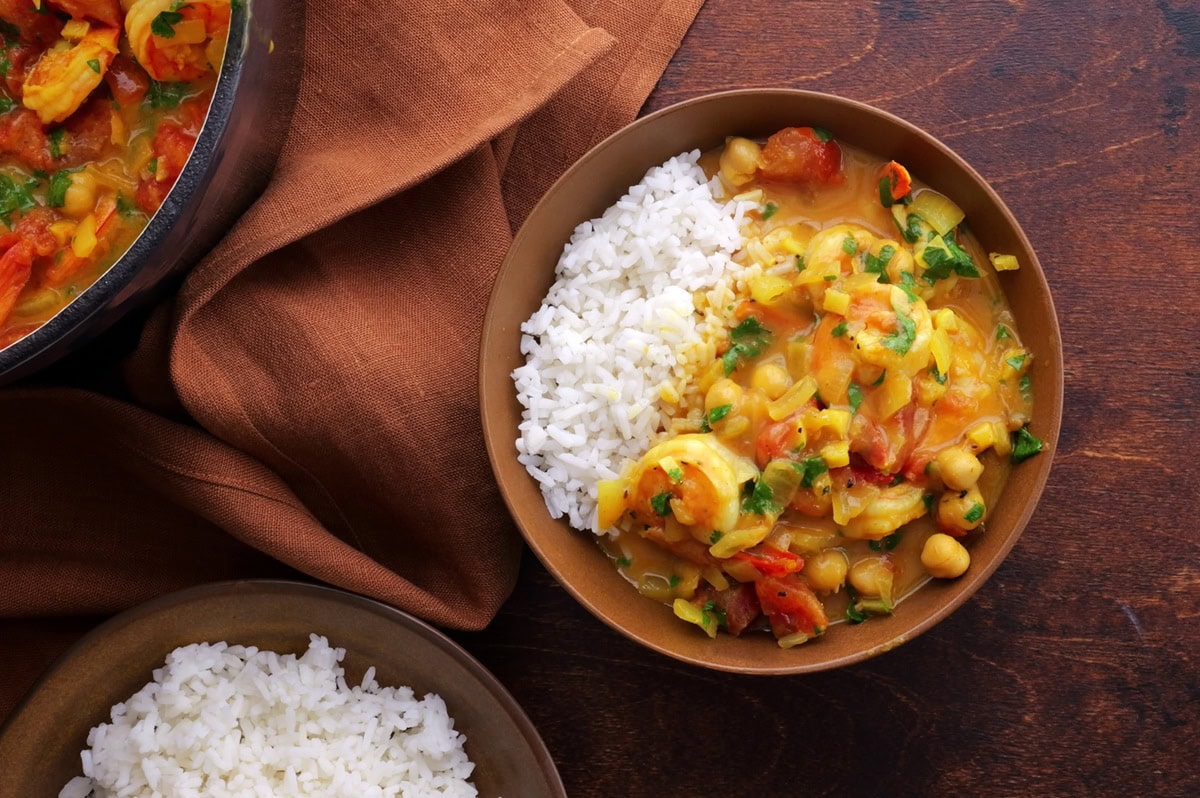 Brown ceramic bowl of shrimp curry on a wooden backdrop.