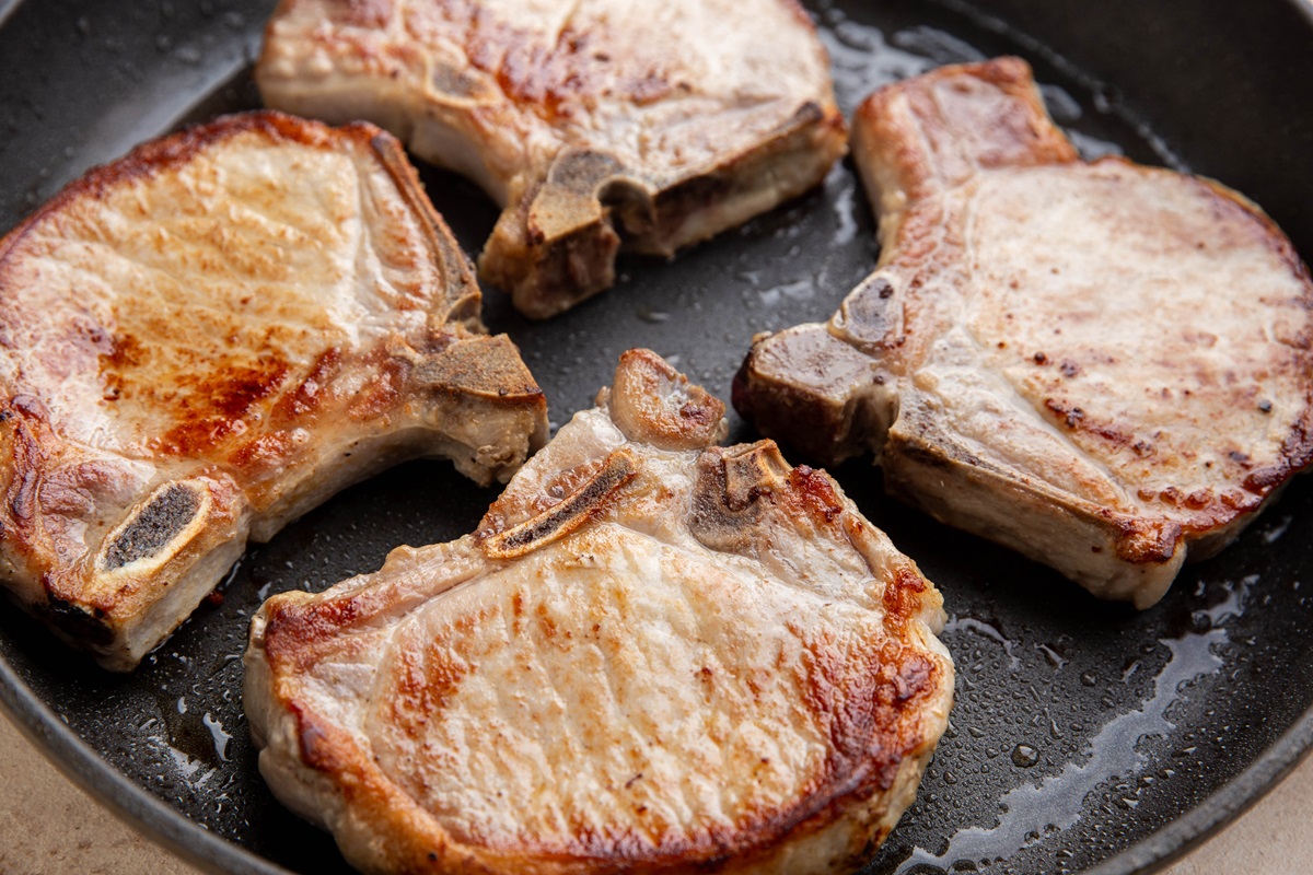 Bone-in pork chops searing in a skillet.