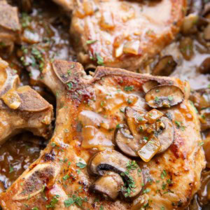 Smothered pork chops with mushroom gravy in a skillet.