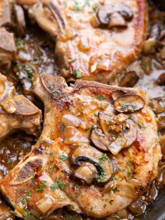 Smothered pork chops with mushroom gravy in a skillet.
