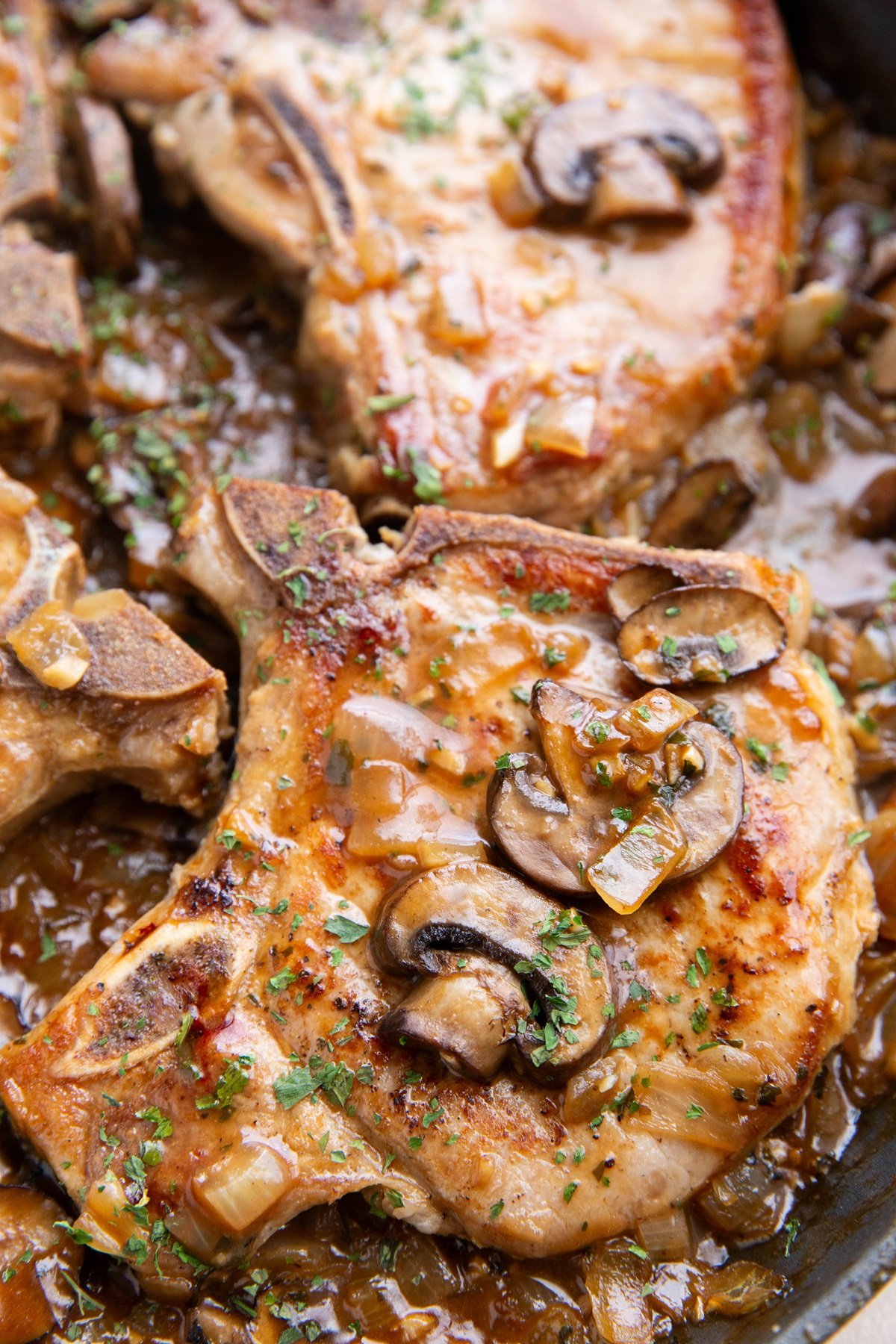 Smothered pork chops with mushroom gravy in a skillet.