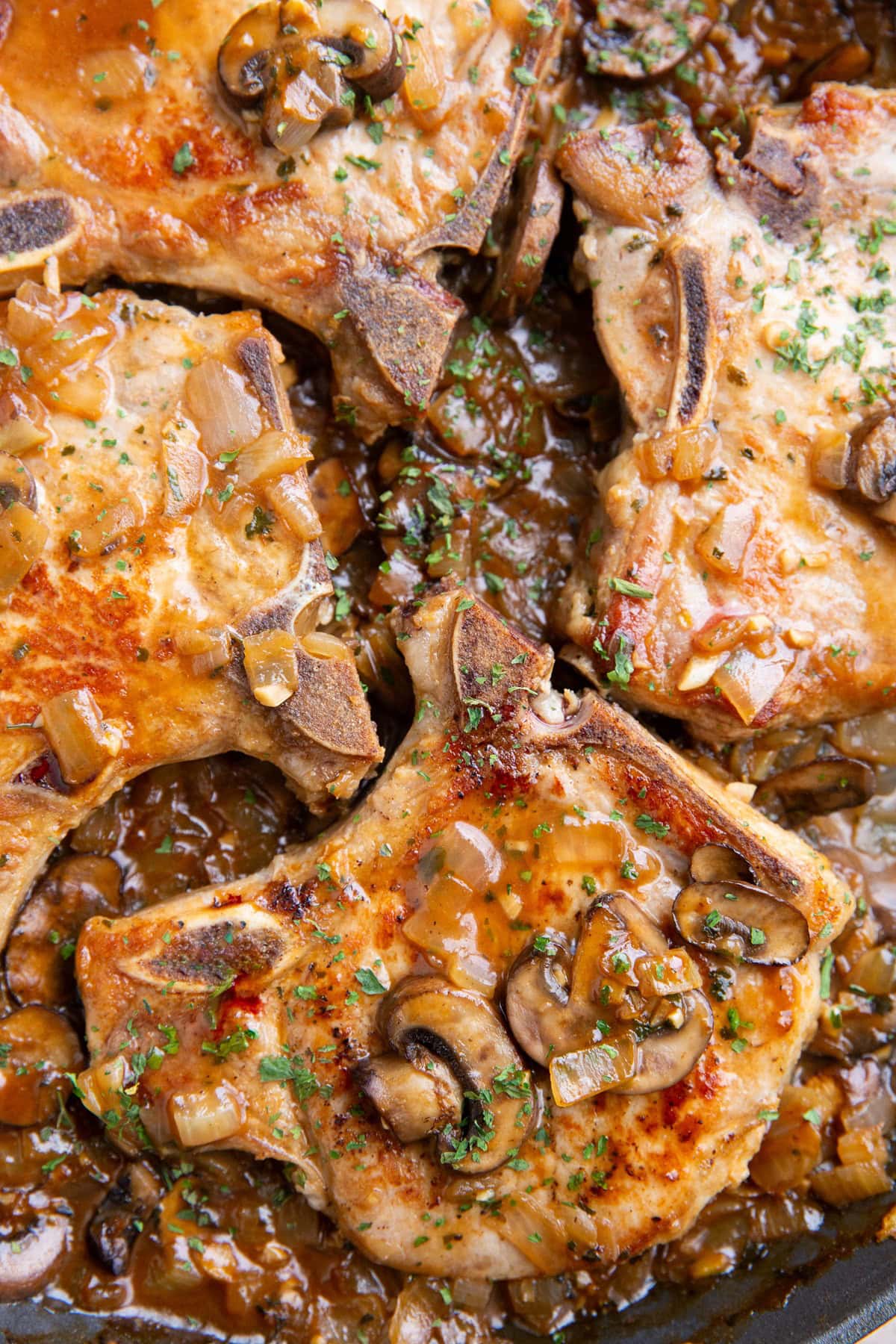 Skillet full of bone in pork chops with brown gravy.