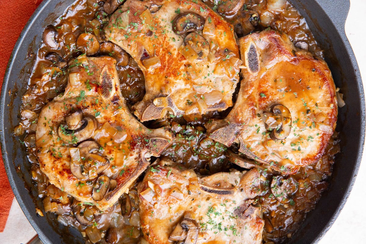 Skillet with four cooked pork chops smothered in gravy.