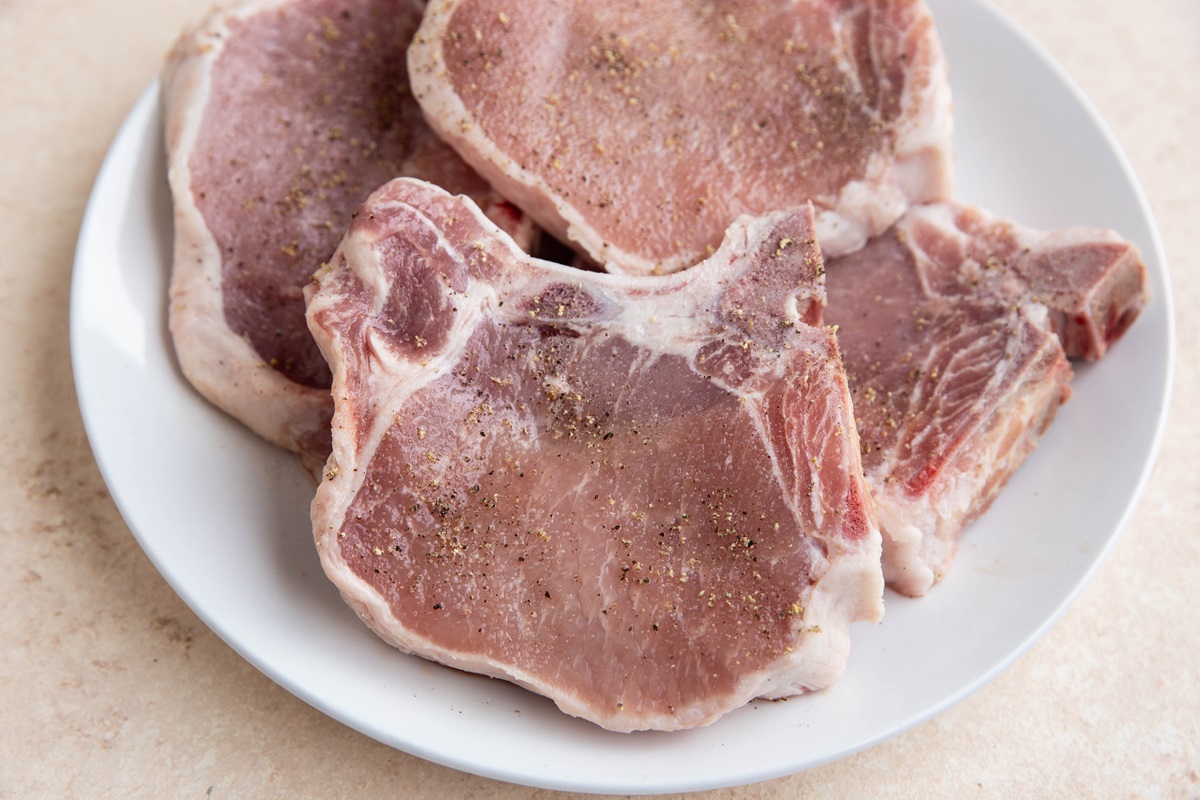 Raw pork chops on a plate seasoned with salt and pepper.
