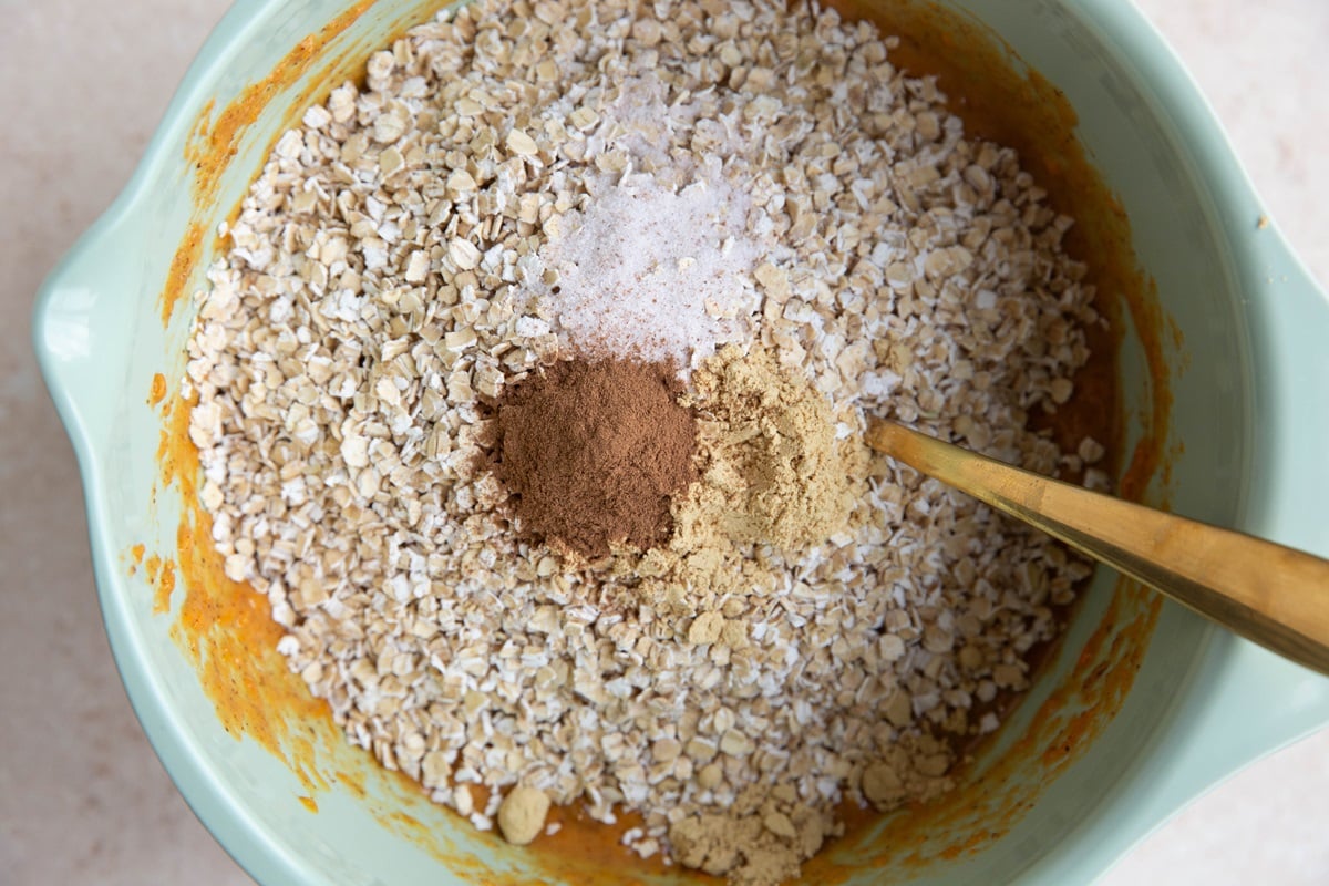 Oats, cinnamon, ground ginger, and sea salt on top of sweet potato wet ingredients to make sweet potato muffin cups.