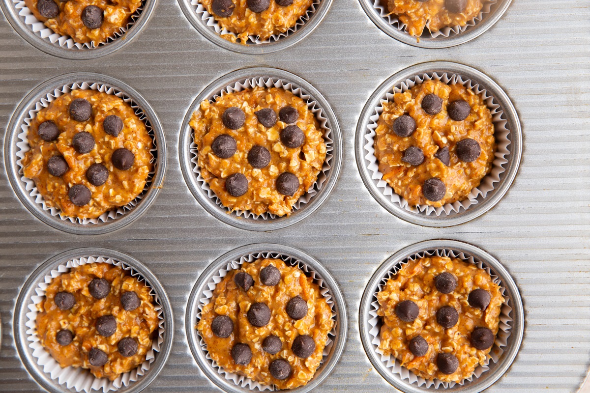 Sweet potato muffin batter in a muffin tin with chocolate chips on top, ready to be baked.