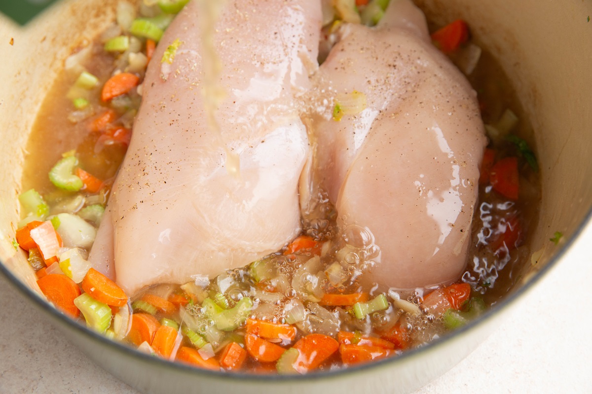 Pouring chicken broth into the pot with the chicken and vegetables.