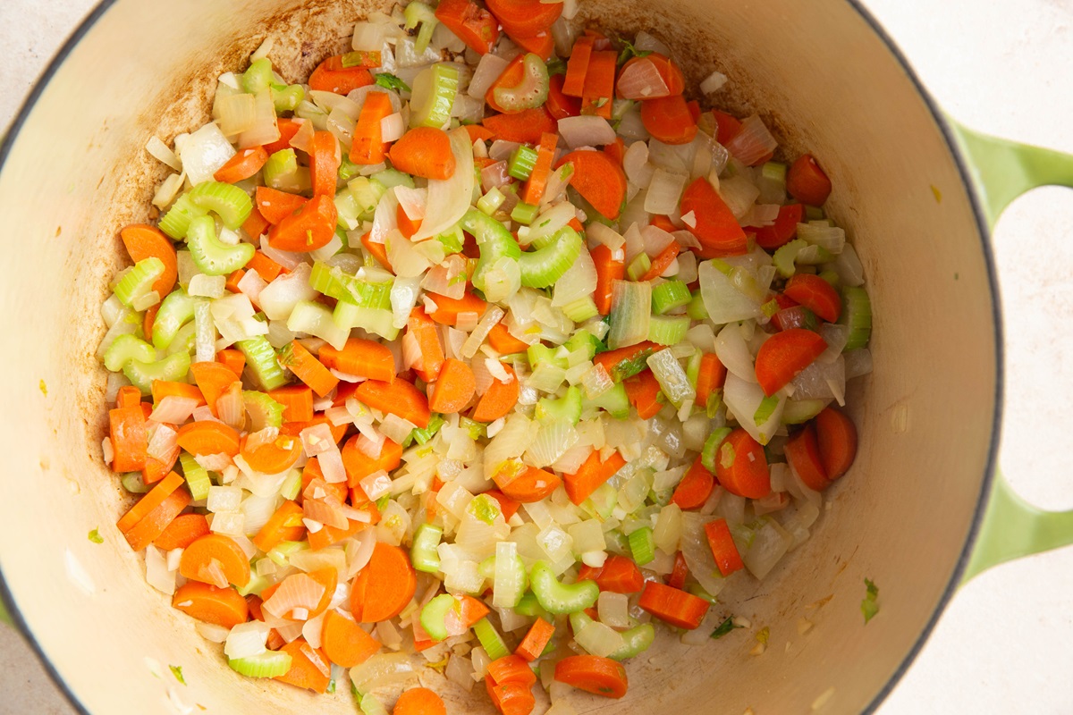 Onion, garlic, celery, and carrots cooking in a large pot.