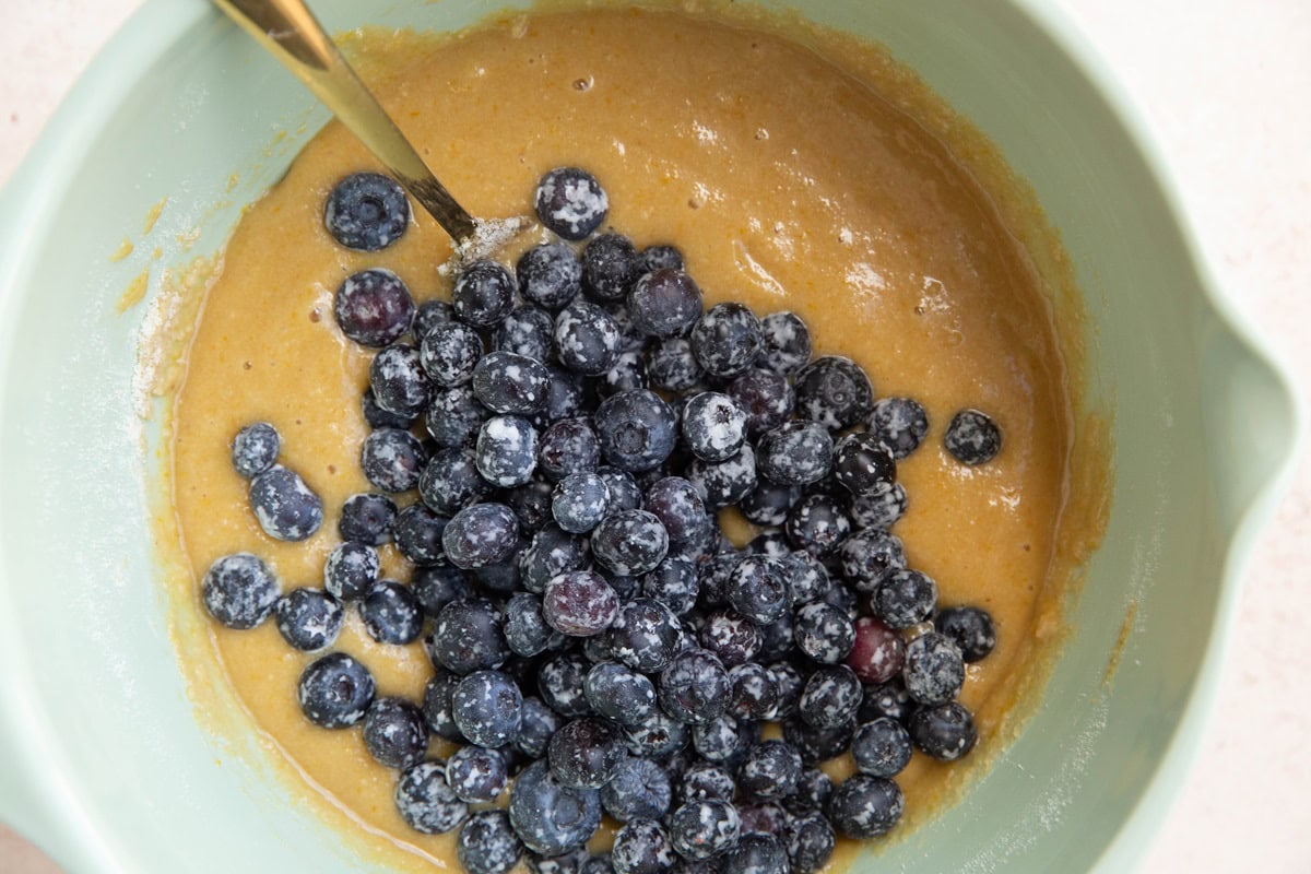 Mixing bowl with almond flour bread batter with blueberries on top, ready to be mixed in.