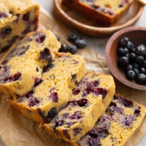 Loaf of blueberry bread on a sheet of parchment paper, ready to eat.