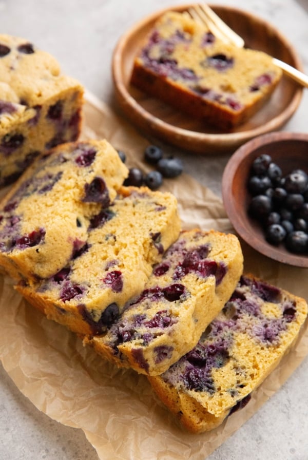 Loaf of blueberry bread on a sheet of parchment paper, ready to eat.