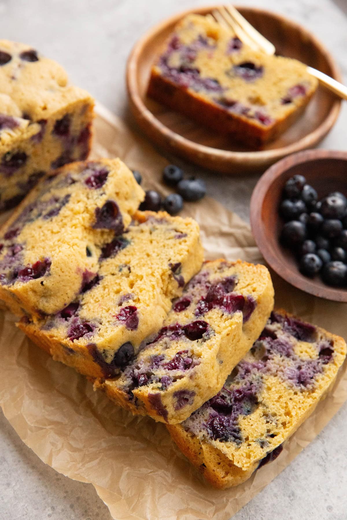 Loaf of blueberry bread on a sheet of parchment paper, ready to eat.